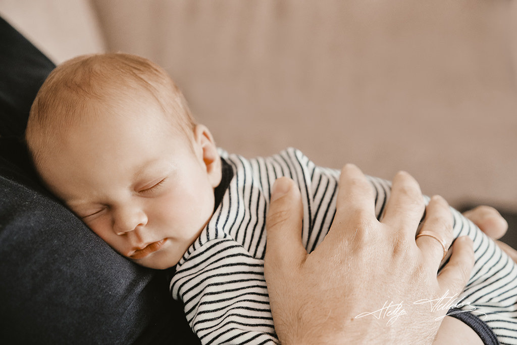 Babyfotoshooting bei dem Baby sicher auf Papas Bauch schlaeft