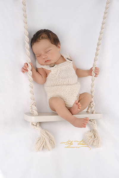 Newborn Fotoshooting in München Harlaching mit Requisite: Ein schlafendes Baby liegt auf einer rustikalen Holzschaukel.